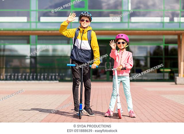 happy school children in helmets riding scooters