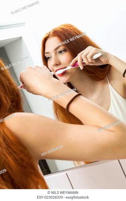 attractive young woman in the morning when brushing your teeth in the mirror in bathroomwith long red hair