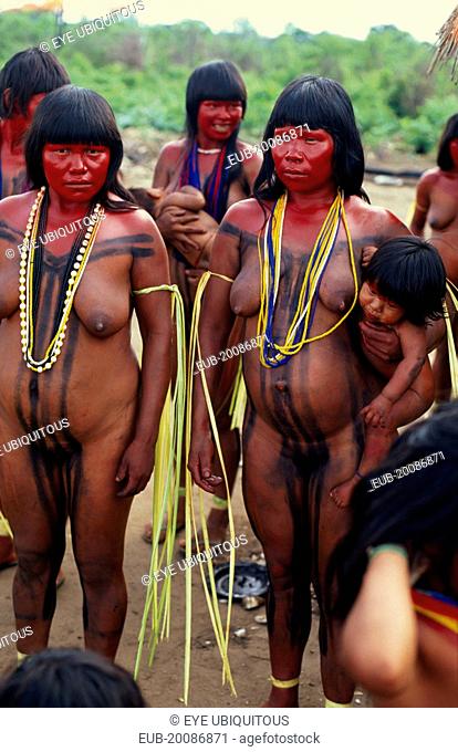 Panara women painted with red karajuru and wearing multi-strands of beads across upper body and long strips of plant fibres tied around upper arms in...