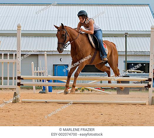 Athletic teen girl jumping a horse over rails
