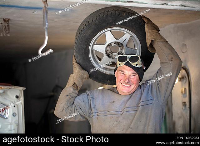 Male auto mechanic in a garage with a car wheel.Fitting tires