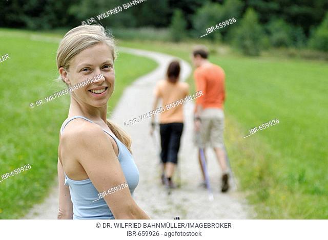 Young woman Nordic walking (ski walking) behind a couple