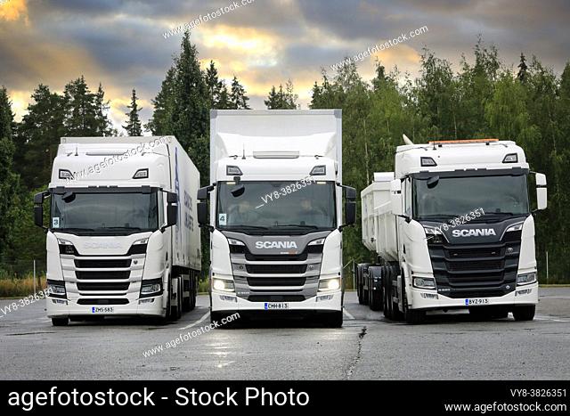 White Scania transport trucks, from left R410, G500 headlights on, R650 parked on yard. Scania in Finland 70 years tour. Turku, Finland. Aug 23, 2019