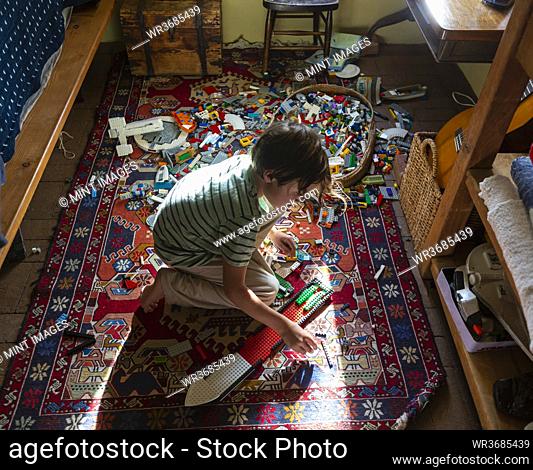 Boy sitting among toys on his bedroom floor in a patch of sunlight