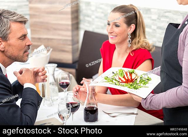 Man sitting with his wife and looking at delicious food which is holding waitress in restaurant