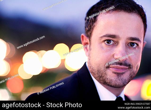 Portrait of businessman at dusk with blurred lights in the background, outdoors in the city, close-up