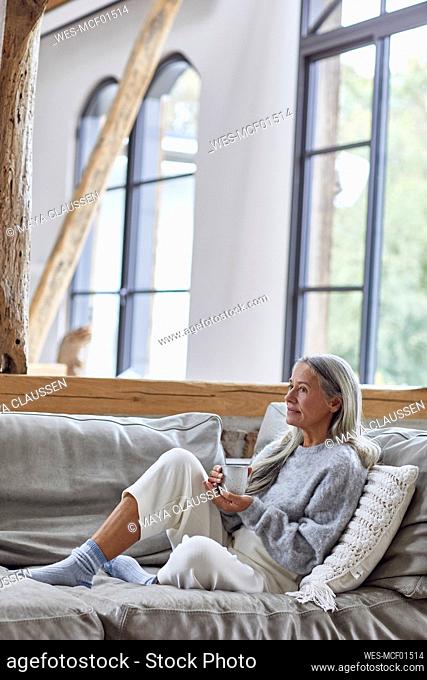Thoughtful mature woman looking away while holding coffee cup at home