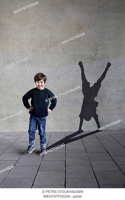 Germany, Duesseldorf, portrait of smiling little boy and shadow of Duesseldorf's cartwheeler on wall