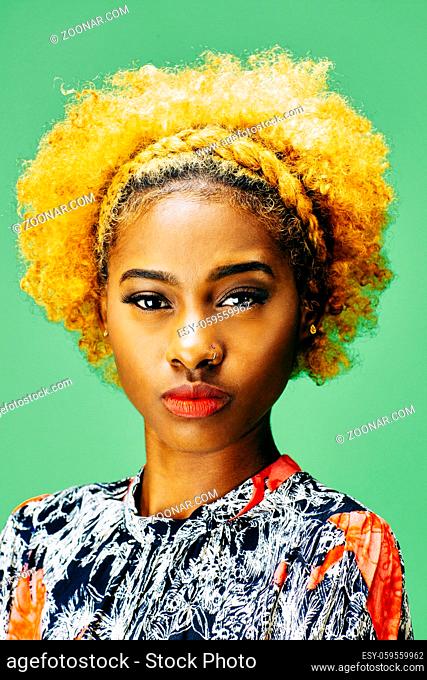 Vertical portrait of a lovely young girl with bleached curly hair, in front of a green background