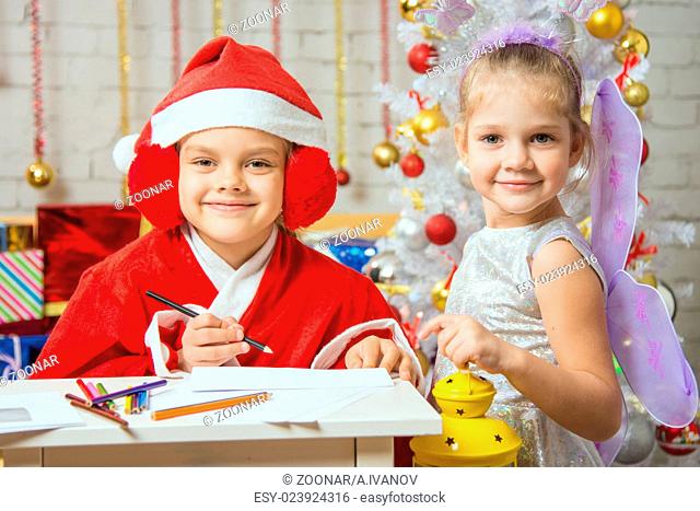 Girl dressed as Santa Claus writing a letter, standing next to a fairy with a flashlight in his hand