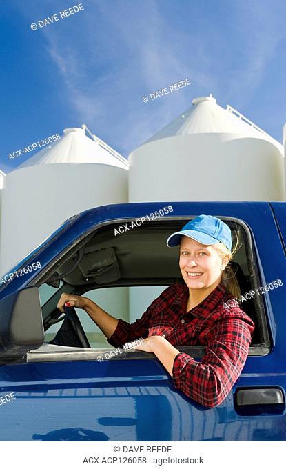 farmgirl in truck next to grain bins in a farmyard, near Lorette, Manitoba