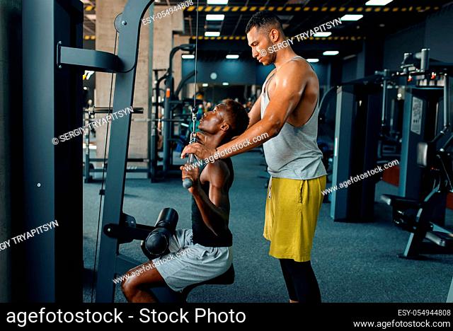 Muscular man and his instructor, exercise with barbell on training in gym. Workout in sport club, healthy lifestyle
