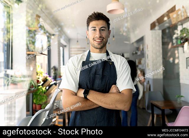 Smiling owner with arms crossed standing in cafe
