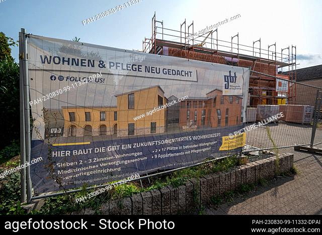 30 August 2023, Rhineland-Palatinate, Hetzerath: A poster of the developer in front of the shell of the building points to the innovative residential project...