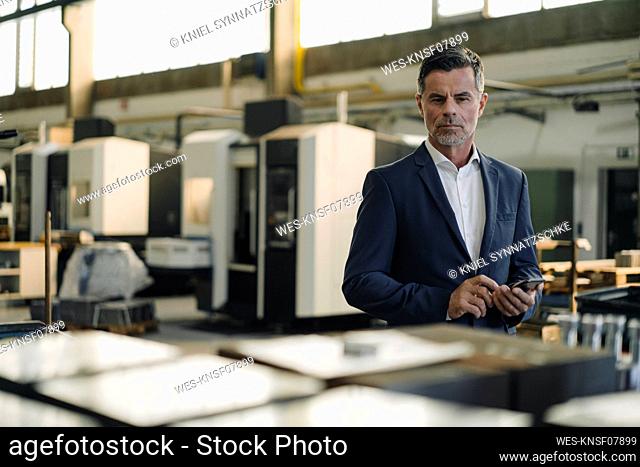 Portrait of a businessman with cell phone in a factory
