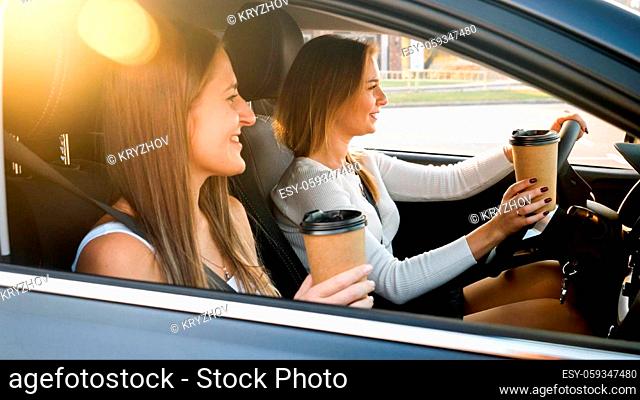 Portrait of two happy smiling girls drinking coffee while riding in car at sunset