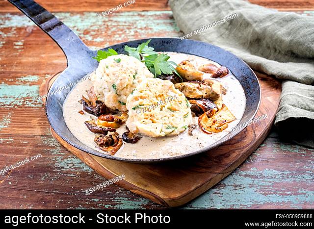 Modern style traditional German cooked porcini mushroom soup with pretzel dumpling and fried potato chips offered as close-up in a wrought-iron pan