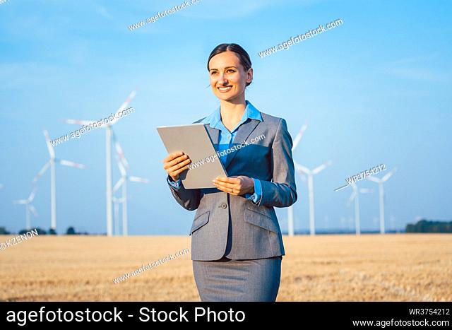 Investor in wind turbines with computer evaluating her investment on site looking pleased
