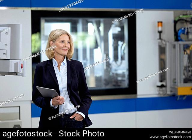 Mature businesswoman with hand in pocket holding digital tablet at factory
