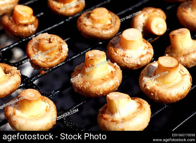 Close up common white champignon mushrooms cooked on BBQ char grill grate, high angle view