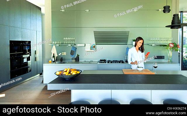 Woman with smart phone eating in modern kitchen