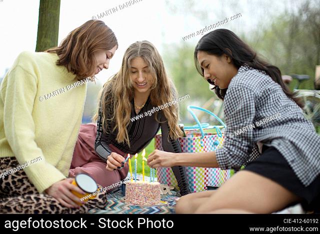 Young women friends celebrating birthday with cake in park
