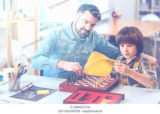 Men-only club. Father and son playing a game of chess sitting at a table in a living room