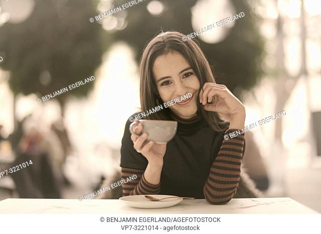 portrait of pleased woman holding coffee cup while enjoying break at table in café, in Munich, Germany