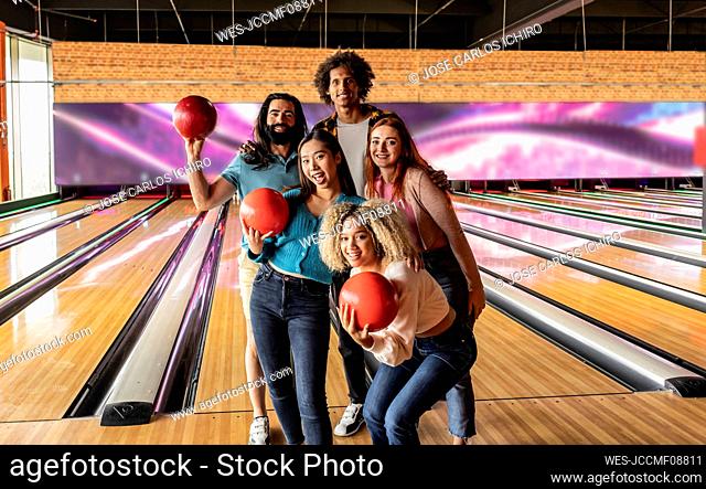 Happy young women and men holding bowling balls at alley