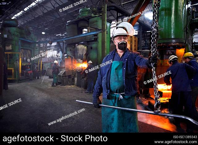 Operative prepares to hook steel billet out of furnace. Team in background using counterblow hammer