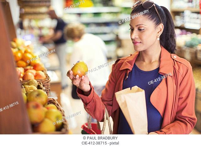 Woman shopping, examining apple in grocery store