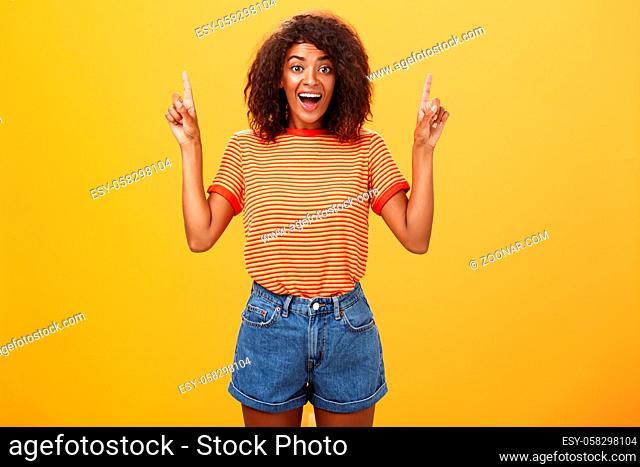 Charmed and impressed african american stylish woman seeing incredible and awesome item on sale raising hands and pointing up with broad grin being excited of...