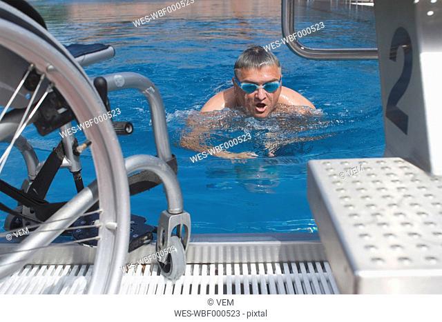 Germany, Ingolstadt, Disabled man in the pool and wheelchair on the brink