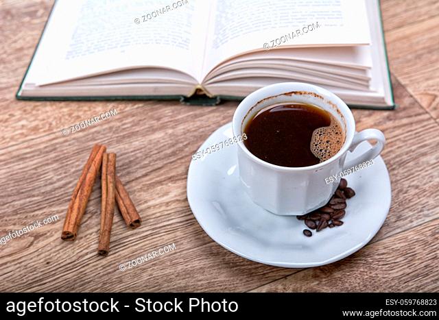 A cup of coffee and cinnamon with a book on a wooden background