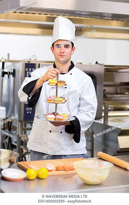 Pastry chef holding tiered cake tray in kitchen