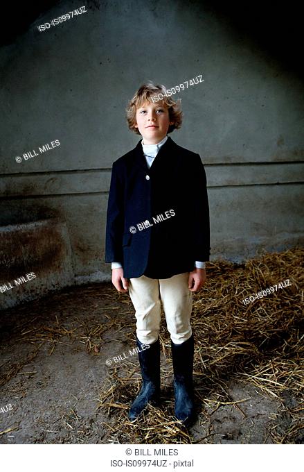Boy standing in horse riding clothes in stable