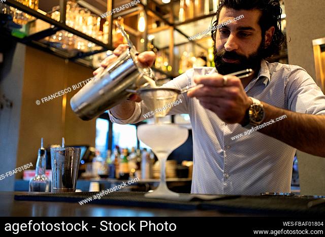Young male bartender pouring drink in glass at bar counter