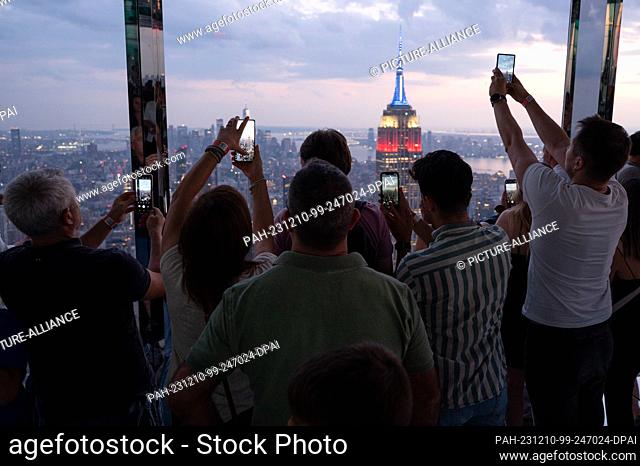 04 September 2023, USA, New York: Visitors photograph the Empire State Building at sunset from the glazed viewing platform The Summit at One Vanderbilt