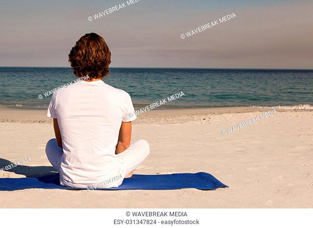 Rear view of man meditating at beach