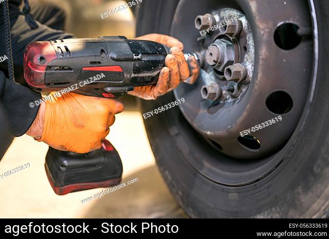 Car mechanic worker doing tire or wheel replacement with electric wrench in garage of repair service station. High quality photo