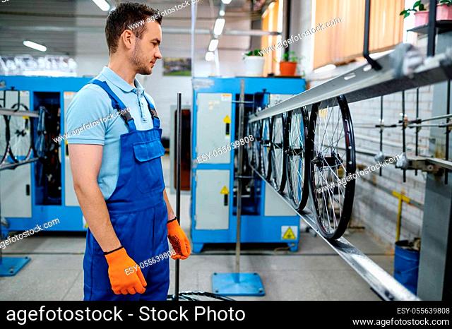 Worker at the assemly line makes bicycle wheels on factory. Bike rims and spokes production in workshop, cycle parts installation
