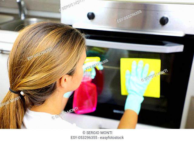 Close up of woman with protective gloves cleaning oven door. Girl polishing kitchen. People, housework, cleaning concept