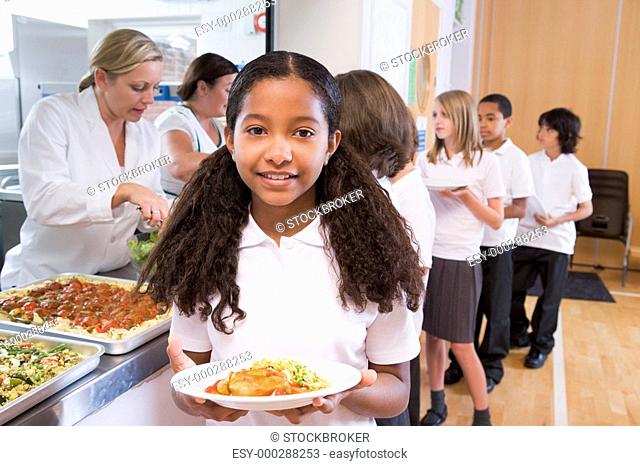 Students in cafeteria line with one holding up her healthy meal looking at camera depth of field