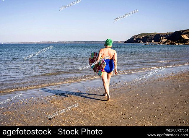 Woman with surfboard walking towards sea at beach