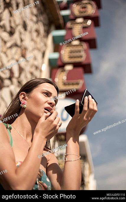 Young woman applying lipstick while looking into palette mirror