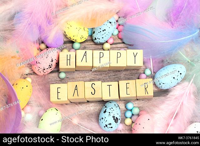 Happy Easter written with wooden cubes surrounded with beautiful pastel colored decorative feathers and eggs, April, Easter, Religion