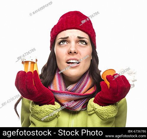 Sick mixed-race woman wearing winter hat and gloves with a tissue holding empty medicine bottle isolated on white