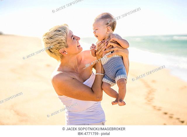 Attractive blond mother playing with 4 months old baby boy on the beach, Portugal