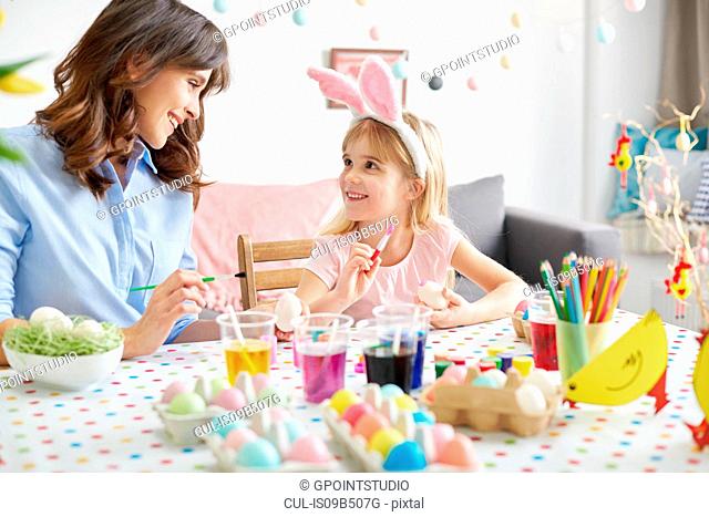 Girl and mother painting easter eggs at table