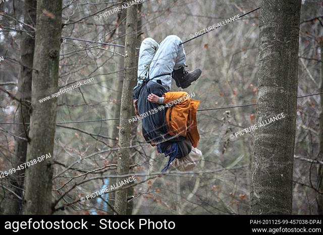 25 November 2020, Hessen, Dannenrod: An activist is dangling headfirst from a rope while police officers try to reach him with a lift truck